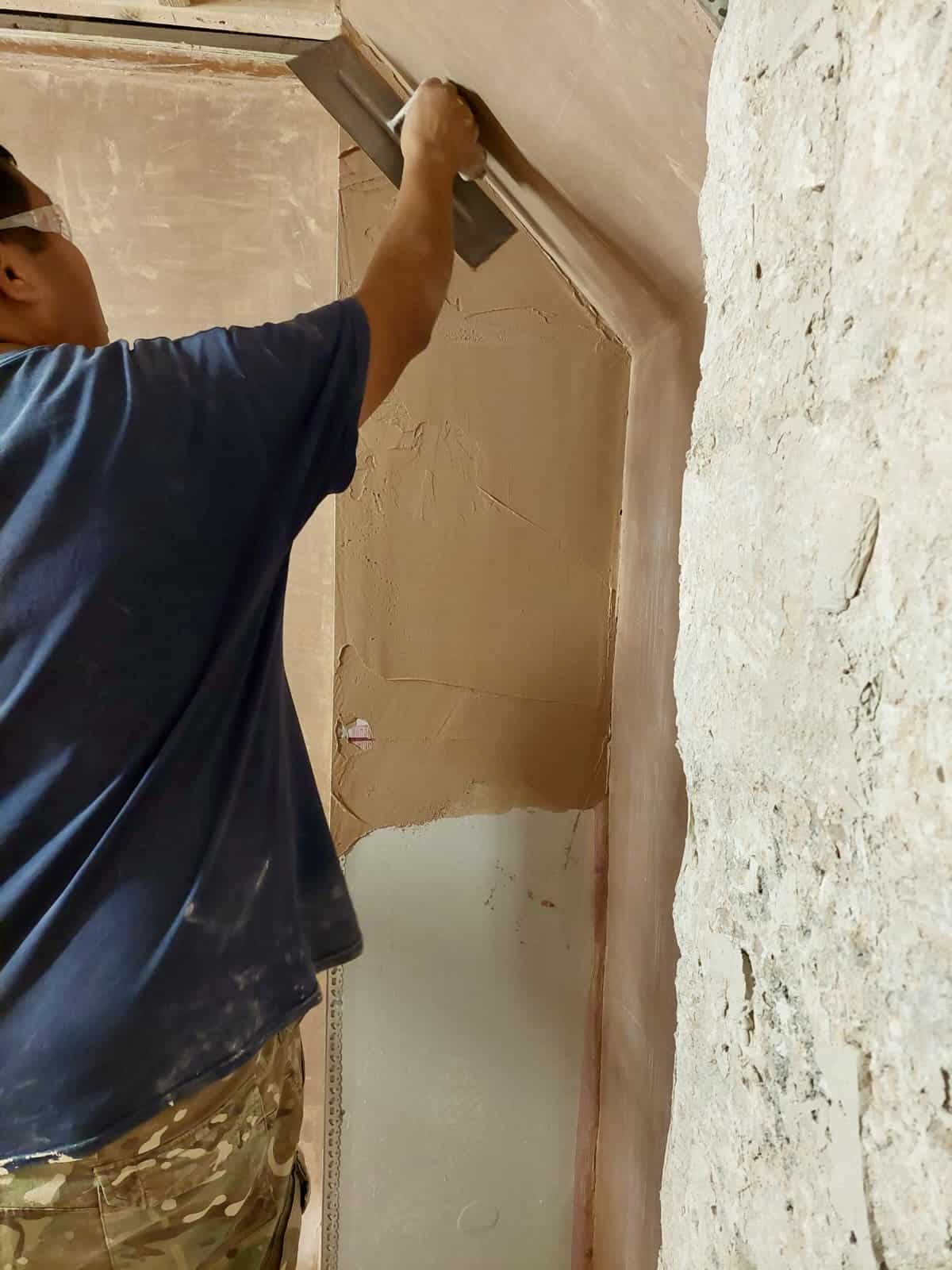 person apply plaster to a wall by a raked ceiling