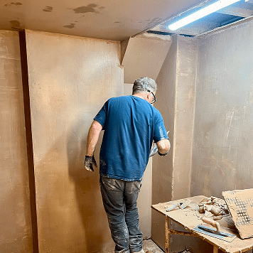 person plastering a section of wall in his bay