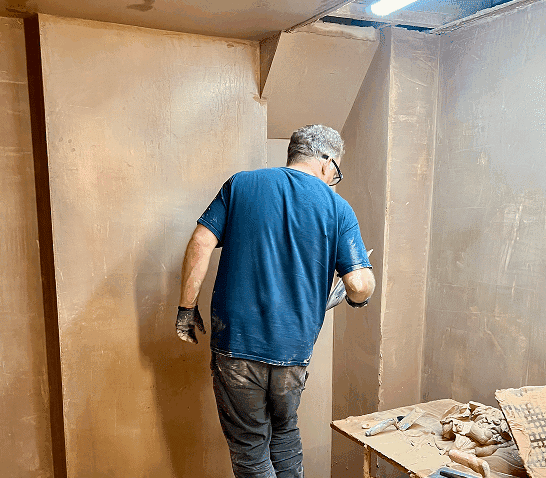 person plastering a section of wall in his bay