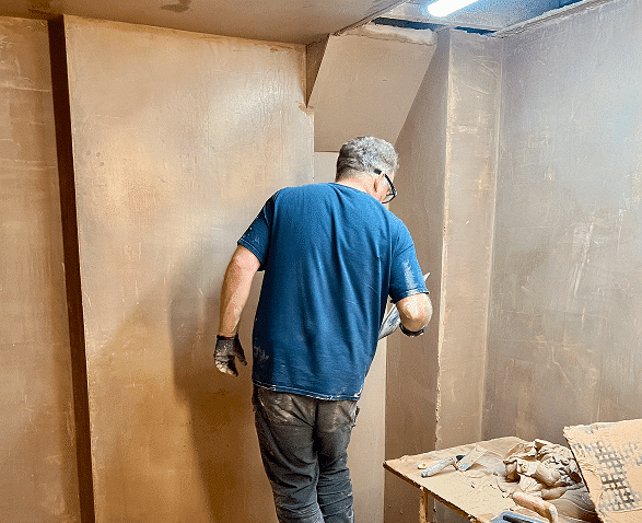 person plastering a section of wall in his bay