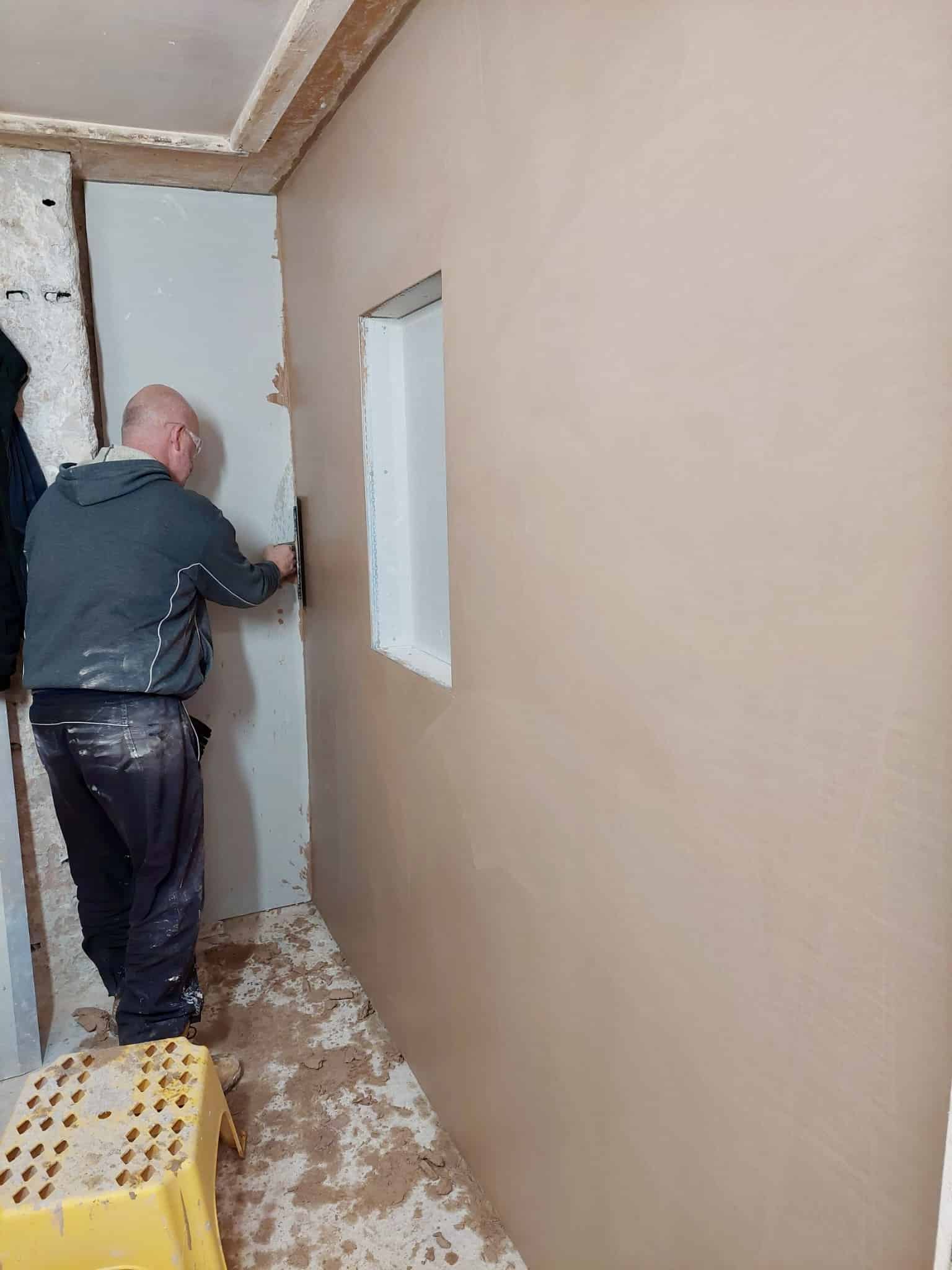 person skimming a wall with a window opening
