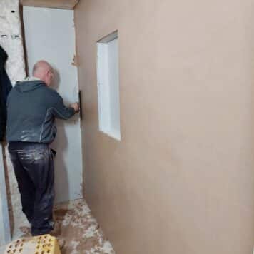 person skimming a wall with a window opening
