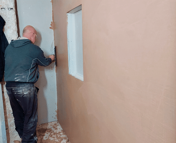 person skimming a wall with a window opening