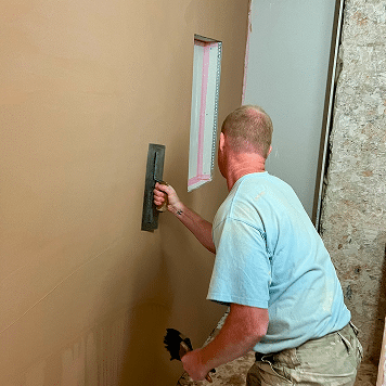 person trowelling off wall