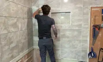 person grouting a wall on his tiling course
